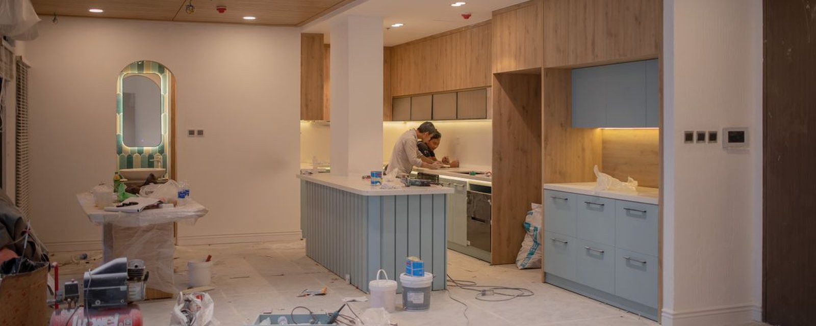 A kitchen mid-renovation — cabinets out, services exposed, dust sheets down