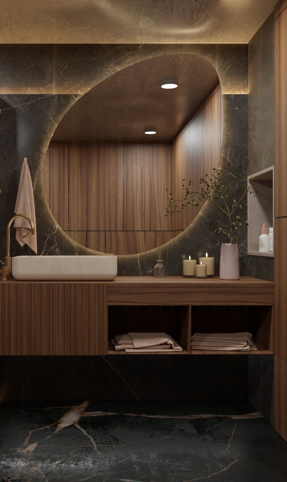 A quiet, dimly lit room finished in dark veined marble and fluted walnut. A large round mirror is lit from behind, a white stone basin sits on a walnut counter with a brass tap, folded towels are stacked on an open shelf below, and three lit candles and a small branch in a pale vase stand at one end.