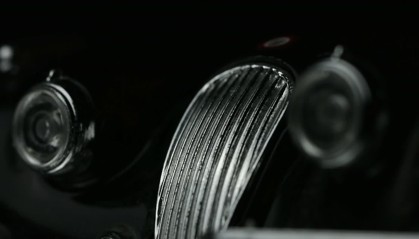 A raking light across the chrome grille and near-black bodywork of a car in the Lustre bay
