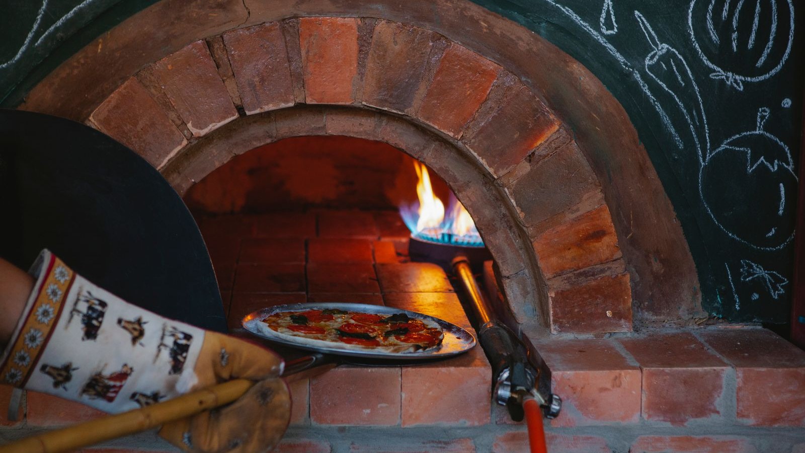A pizza slid into the brick oven on a peel, flames at the back
