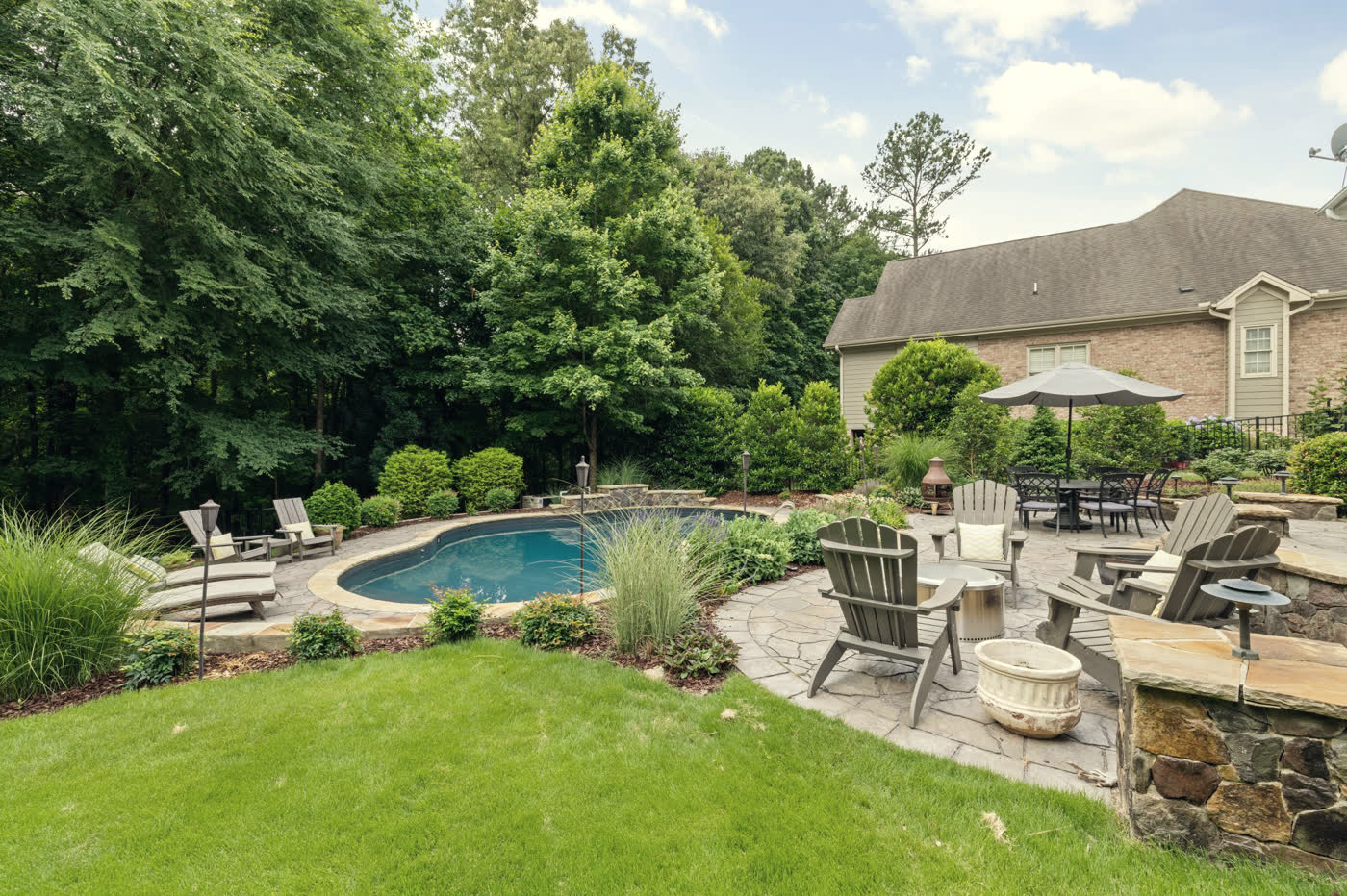 A kidney-shaped in-ground pool with irregular flagstone coping, a flagstone patio carrying chairs and a fire bowl, and a dry-laid fieldstone seating wall running across the foreground.